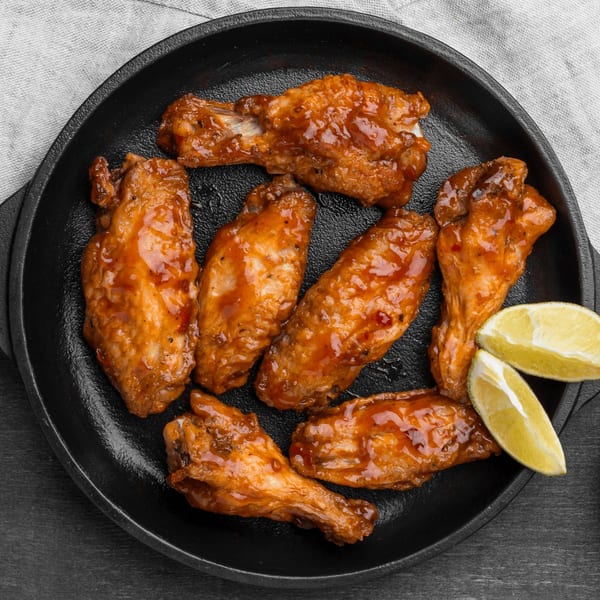 Seven glazed chicken wings with two lime wedges in a black cast iron pan.